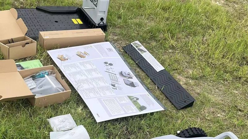 Everything in the VERDA box laid out on a lawn: the robot, the base station plate and the printed setup guide